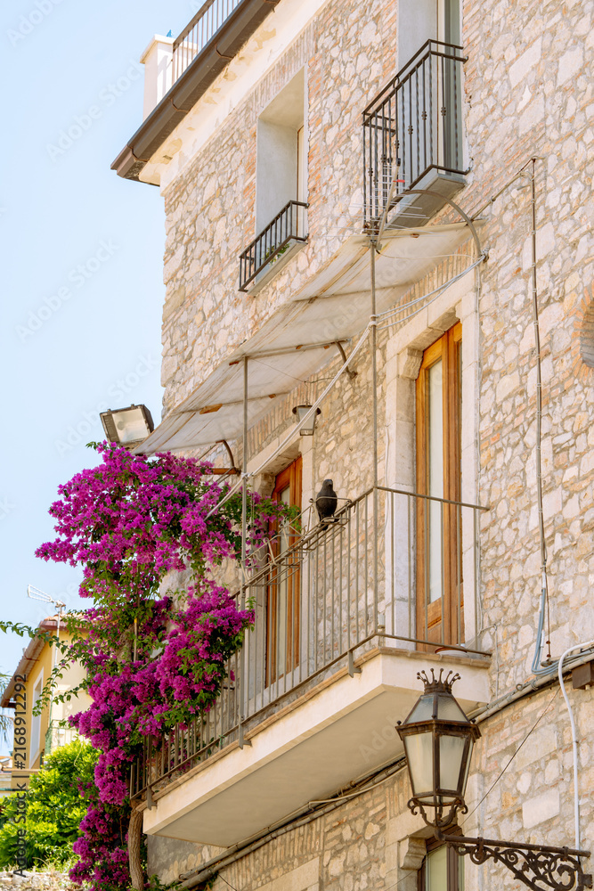 Fototapeta premium Traditional Sicilian stone facade with bright purple bougainvillea flowers and wrought iron balconies