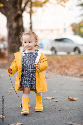 Cuadro en lienzo Cute kid girl 2-3 year old wearing yellow raincoat and rubber boots outdoors