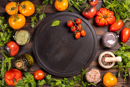 Fresh vegetables, herbs, spices, and olive oil surrounding a dark wood board