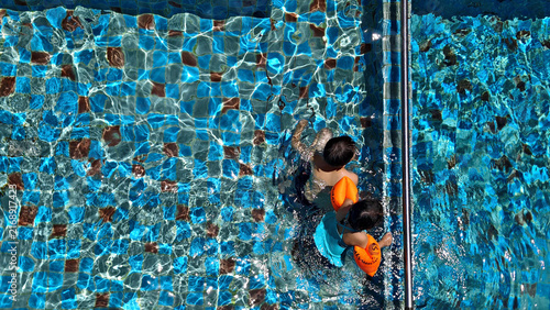 Two children swimming with orange arm floaties in a blue tiled pool