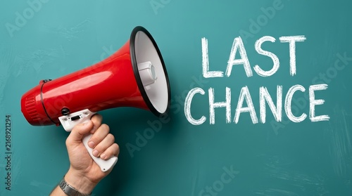 A hand holding a red and white megaphone making a last chance announcement.