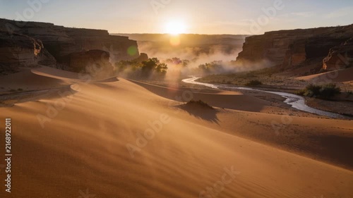 Shifting dune ridge shedding sand streaks down slip face under steady breeze at sunrise haze rising