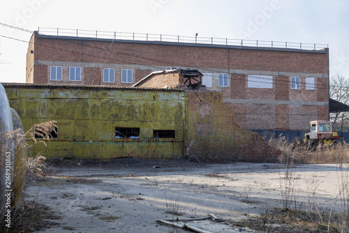 Fotografie Abandoned building with damaged brick wall and empty ground near industrial site