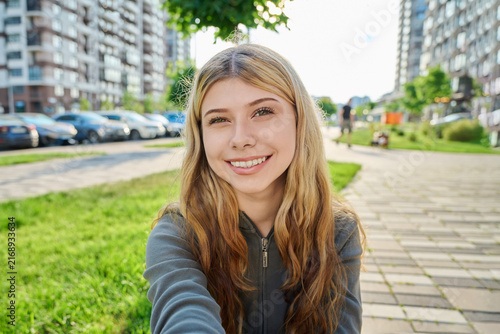 Young attractive woman taking a selfie outdoors in modern city street on sunny summer day