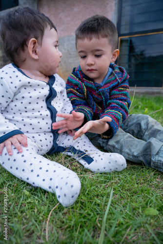 Little brothers sharing a hand game while sitting on the lawn outdoors.