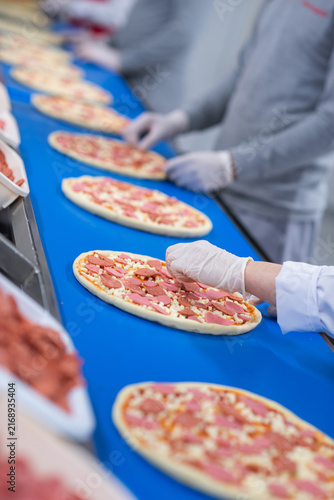 Workers Placing Toppings on Pizzas in Factory
