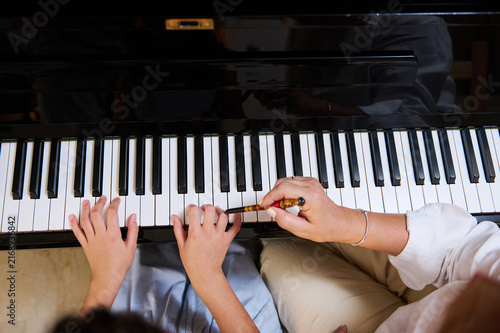Piano teacher guiding child's hands during a piano lesson in a music class