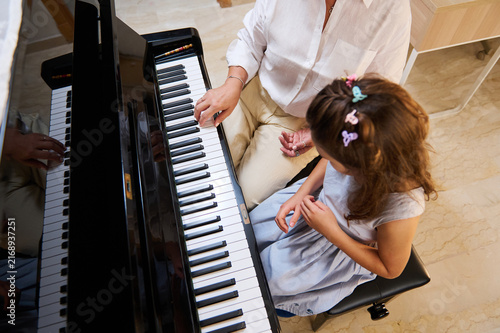 Woman piano teacher giving a piano lesson to a young girl at home