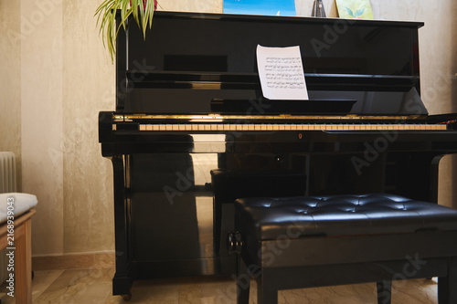 Black upright piano with sheet music and bench in cozy living room