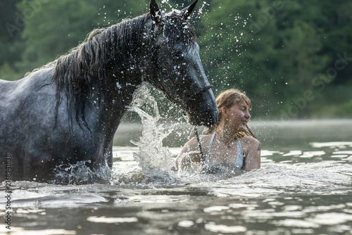 Frau badet mit Pferd im See