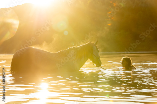 Frau badet mit Pferd im See