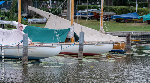 Quadro su tela Traditional sailing boats lined up at mooring posts on Wroxham Broad, Norfolk Broads, with calm waters and a peaceful summer scene