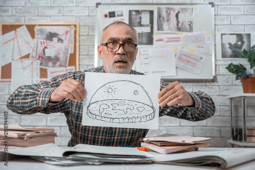Fotografie Senior flat Earth conspiracy theorist holding a hand drawn diagram of the world