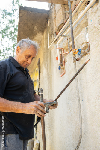 Senior man measuring copper pieces before soldering for a country house plumbing installation.