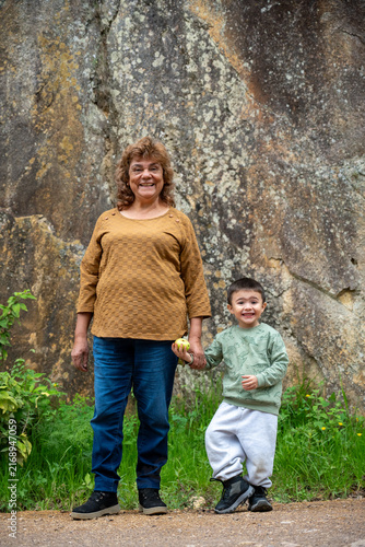 Grandmother and grandson making funny and matching expressions while holding hands against a rock wall.