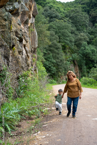 Grandmother and grandson enjoying a walk on a dirt trail with trees and large rocks in Mineral del Chico, Mexico.