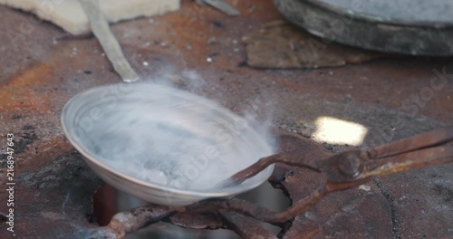 Coppersmith tinning and coating copper bowl over fire with tin and sal ammoniac in traditional workshop