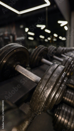 Cuadro en lienzo Row of heavy dumbbells on a rack in a dimly lit gym
