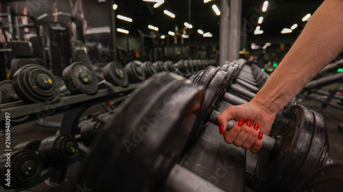 Canvas Print Woman's hand with red nails picking up a dumbbell from a rack in a gym