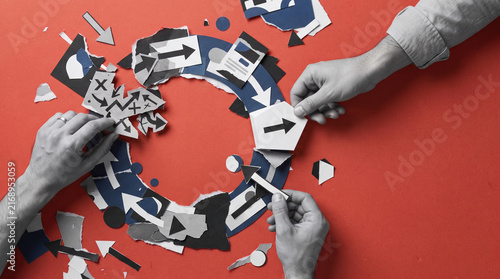 Grayscale hands arranging torn paper arrows and geometric cards along a circular path on a red background