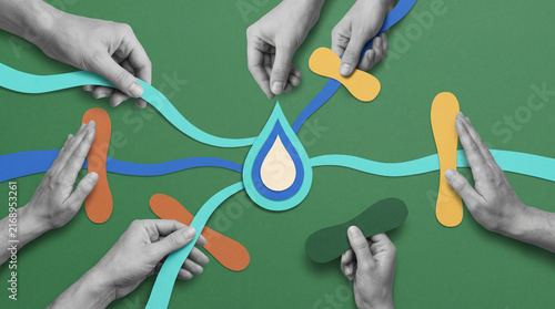 Grayscale hands arranging colorful paper shapes and flowing ribbons around a central droplet on green background