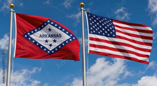 Arkansas state flag and US flag flying together on poles against a bright blue sky with scattered clouds