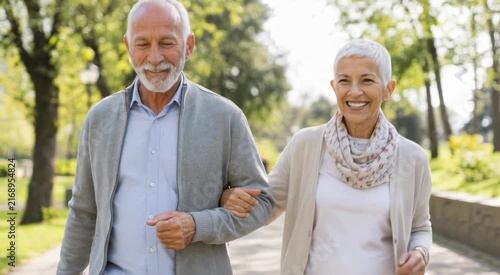 Smiling retired senior couple walking arm-in-arm in a sunny park