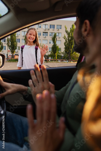 Фотография Happy schoolgirl saying goodbye to parents through car window after arriving at
