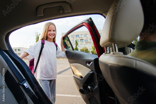 Happy girl opening back door of family car and smiling during afternoon school pickup, showing loving everyday family routine