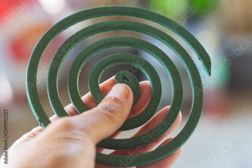 Fotografía Human hand holding a green spiral mosquito repellent coil close-up against a sof