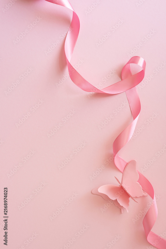 Fototapeta premium Pink ribbon and paper butterfly on soft vertical pink background for Breast Cancer Awareness Month support and hope