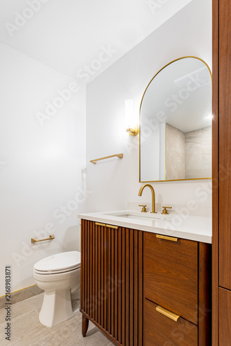 Modern bathroom interior with wood vanity, arched mirror, gold fixtures and white countertop