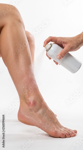 Applying foot spray to a leg with tanned skin. The person's skin is smooth, and the spray is creating a mist around the lower leg and ankle