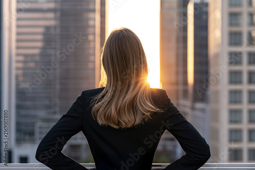 Businesswoman seen from behind, looking at office buildings with sunbeams in the background