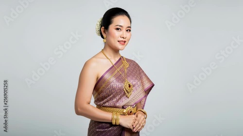 Elegance Embodied: A serene woman adorned in traditional Thai silk attire and exquisite gold jewelry, posing gracefully. Her hair is elegantly styled with a white flower.