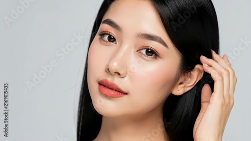 Radiant Beauty: A young Asian woman with flowing black hair and captivating eyes gazes into the camera, her flawless complexion and gentle smile radiating confidence and allure.