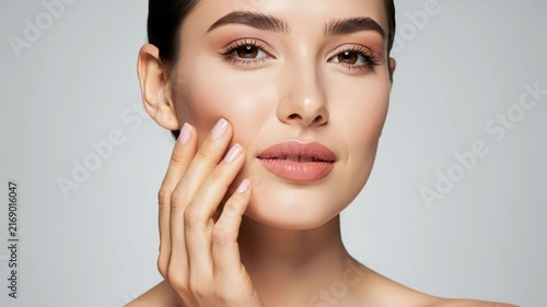 Portrait of Radiant Beauty: A captivating young woman with flawless skin and soft, natural makeup gently touches her cheek, exuding a sense of serene elegance and self-care.
