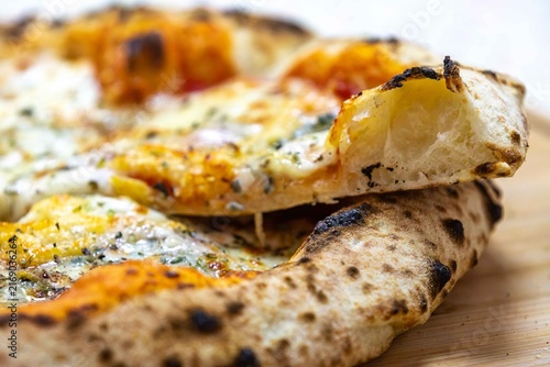 Neapolitan-style four-cheese pizza with leopard-spotted puffy crust and open airy crumb, sliced on a bamboo board — naturally leavened long-fermentation dough.