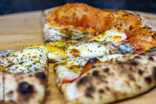 Neapolitan-style four-cheese pizza with leopard-spotted puffy crust and open airy crumb, sliced on a bamboo board — naturally leavened long-fermentation dough.