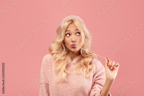 Canvastavla Smiling Young Caucasian Woman With Blonde Hair Chewing Gum While Making Playful Face In Studio With Pink Background, Enjoying Casual Moment And Having Fun