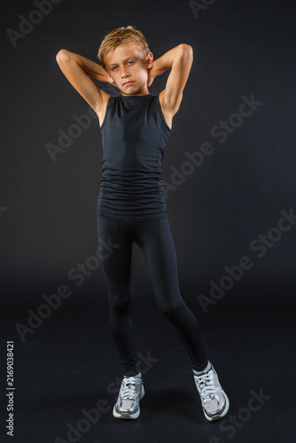 Young boy athlete posing in black athletic running tights against a black background