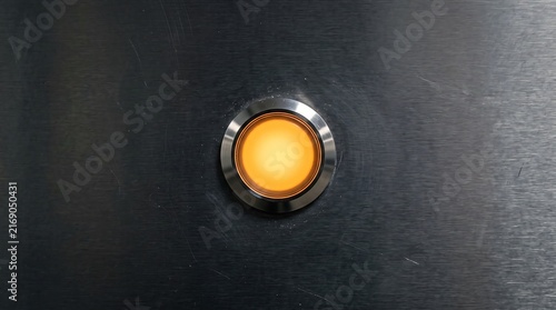 Glowing amber industrial button on dark brushed metal surface