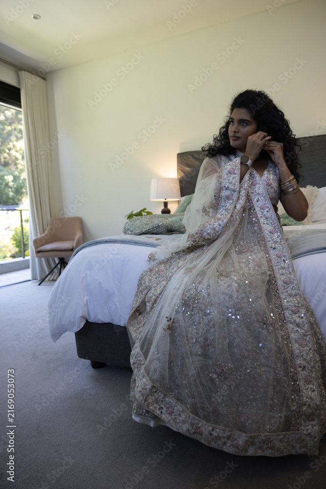 Fototapeta premium Embroidered sequined gown is resting on bed near lamp while sheer dupatta is cascading