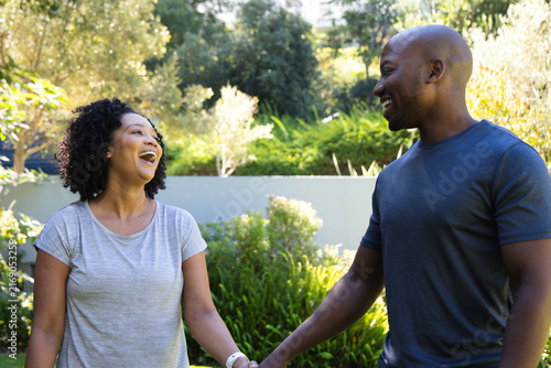 Obraz na płótnie African American couple facing each other, laughing and holding hands in sunlit