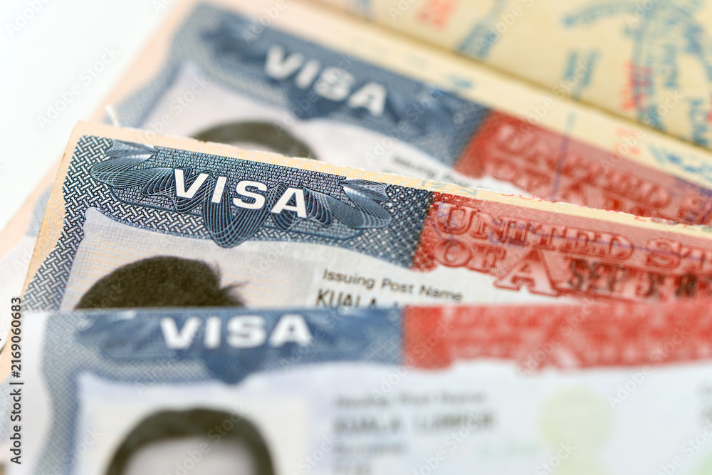 Naklejka premium Three United States visa stamp inside an open passport document, held by a hand, for immigration, international travel, border security, visa application, and citizenship topics.