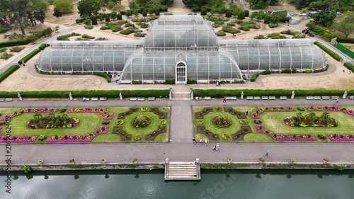 Symmetrical Victorian palm house faces its formal parterre of flower beds across a lake in botanic gardens