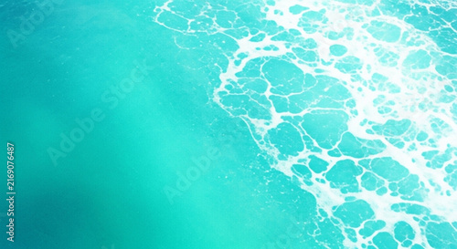 An abstract aerial view showcases swirling turquoise water and frothy white sea foam patterns high-quality