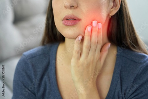 Young woman holding her cheek while suffering from painful jaw bruxism due to night stress
