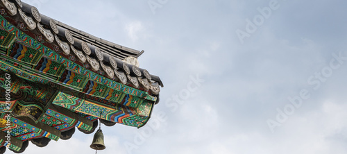Fotografie Ornate double eaves with colorful dancheong paint and wind chime on tiled roof of traditional Korean Buddhist temple against sky with copy space