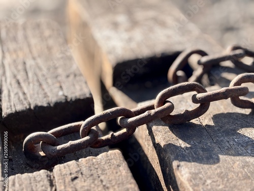 Close up of old rusty metal chain on weathered wooden planks. Vintage industrial texture and strong connection concept background.